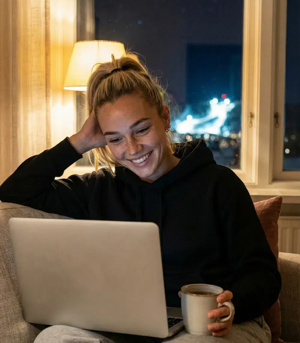 Glad och nöjd kvinna framför sin fungerande laptop. Kontakta PG HemTeknik för hembesök i Östersund.